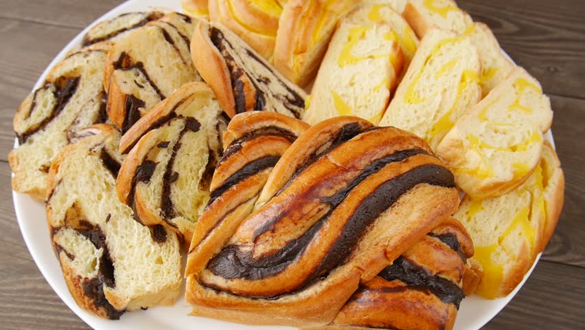 Assortment of fresh sweet bread with chocolate and cheese filling rotating on a white plate.