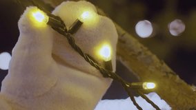 Close up of winter-gloved hand touching glowing string lights wrapped around a tree branch, soft golden bokeh lights in the background create a cozy and festive ambiance - Powered by Shutterstock - Get 15% off with code: PIKWIZARD15