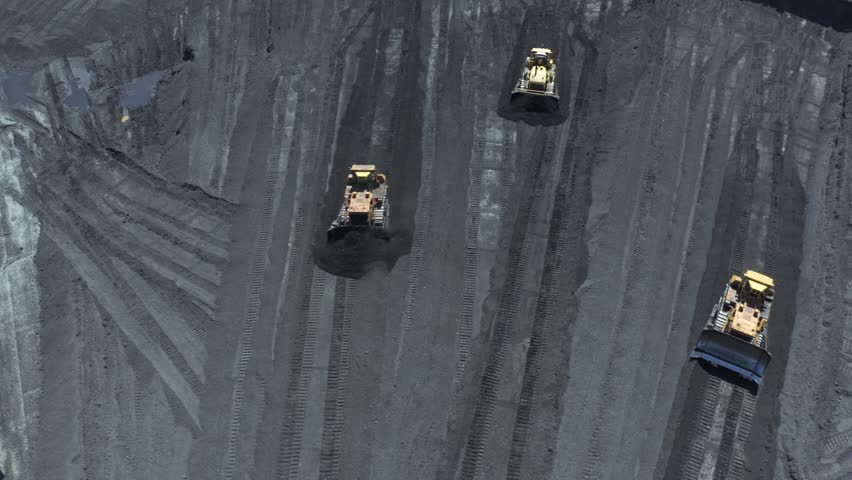 Aerial view of bulldozers directing coal at thermal power plant during daylight operations for energy production