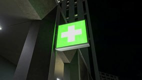 Close-up night shot of an illuminated green pharmacy cross sign on a modern building facade. The glowing medical symbol represents healthcare, medicine, and pharmacy services. Urban city environment - Powered by Shutterstock - Get 15% off with code: PIKWIZARD15