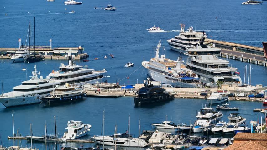 View of boats and yachts docked in the Monaco marina, surrounded by luxury buildings and calm blue water on a sunny day in the French Riviera.