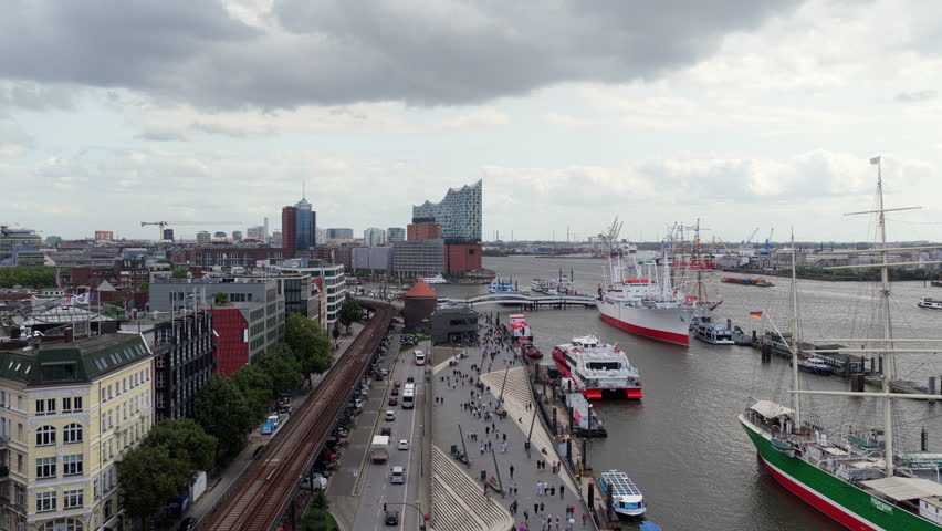 Aerial view of Hamburg port with boats docked and the Elbphilharmonie concert hall. Tourists walk on waterfront promenade