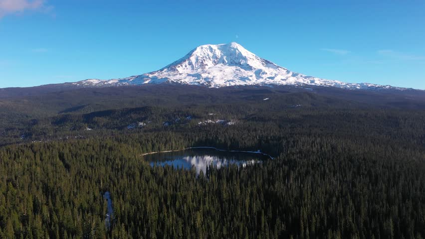 4K aerial drone footage of Takhlakh Lake and snow covered Mount Adams in Washington State USA during late fall early winter. Scenic reflection of mountain in calm water surrounded by evergreen forest 