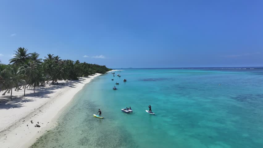 Aerial view of people enjoying the turquoise waters near the sandy beach under the bright sun, Naavaidhoo, Haa Dhaalu City, Maldives.