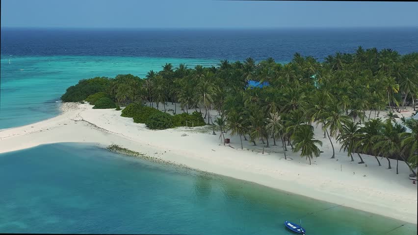 Aerial view of an island with boats near the sandy beach, lush palm trees, and buildings contrasting with the turquoise waters, Naavaidhoo, Haa Dhaalu City, Maldives.