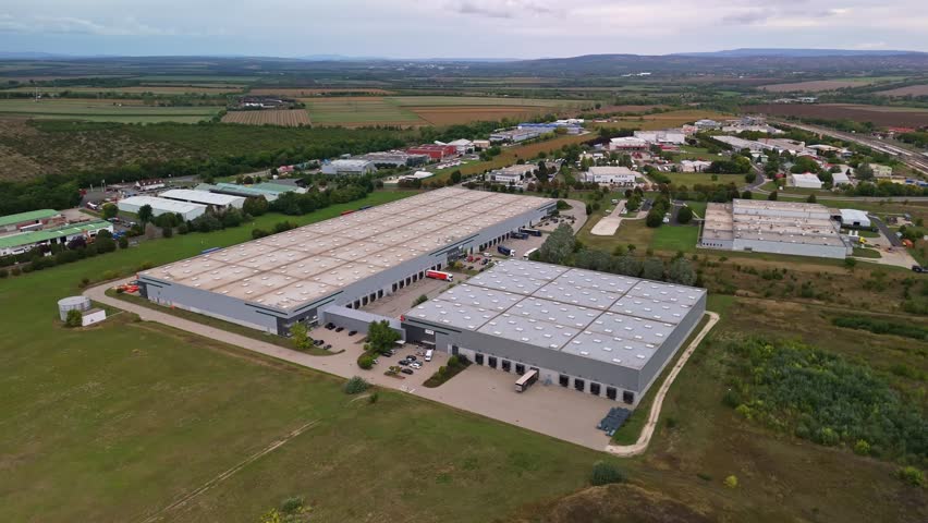 Aerial view of an industrial park on the outskirts of Százhalombatta, Hungary, with loading trucks and hangar buildings along the road 6.