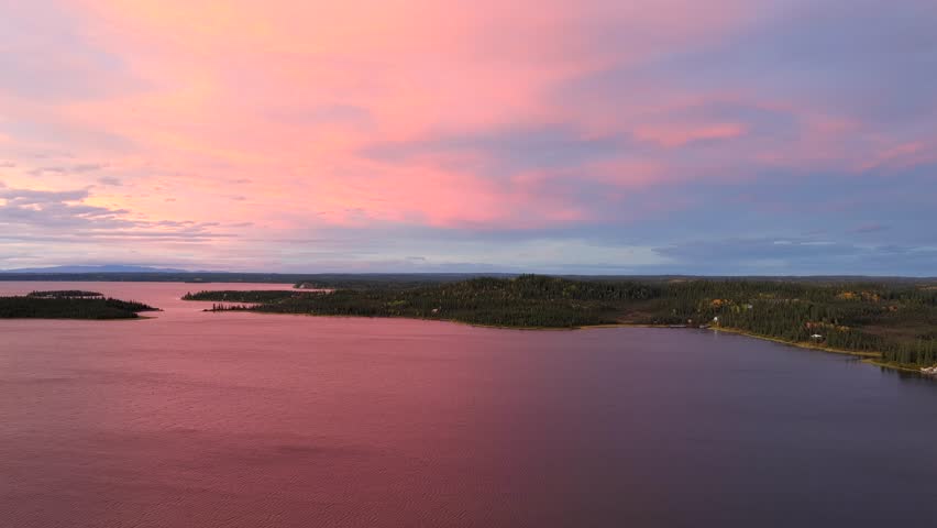 Aerial view of the tranquil Lake Louise under a pastel sky, reflecting hues of pink and purple amidst the dark forest, Lake Louise, Alaska, United States.