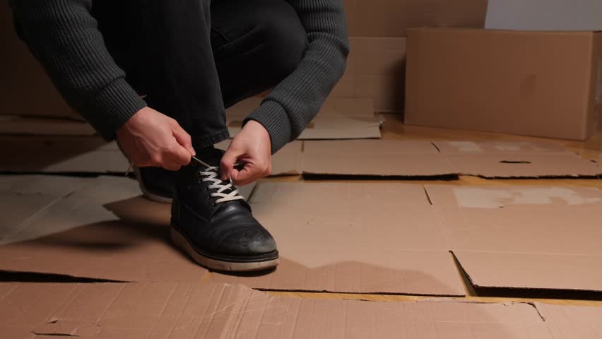 preparing to depart, lacing shoes before leaving scene, person fastening shoelaces on box 