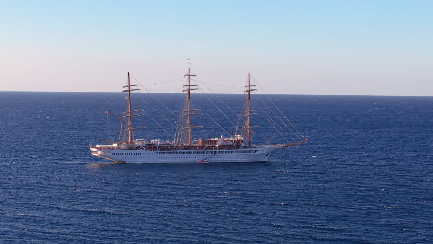 Aerial elegant threemasted sailing ship cruising at dawn by rocky island shores amid tranquil blue seas. Calvi. Corsica. France