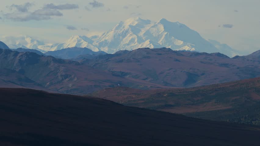 Aerial view of the snow-capped peaks of Denali National Park rise majestically over the rugged, autumnal landscape in shades of brown, Denali, Alaska, United States.