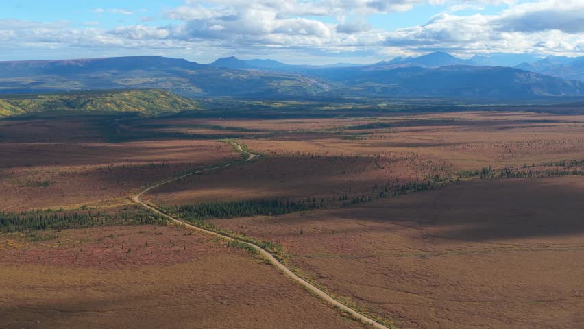 Aerial view of a winding road cutting through the landscape, with mountains in the distance under a partly cloudy sky, Healy, Alaska, United States.