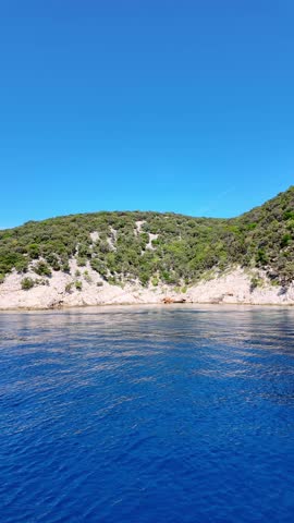 Pristine coastline panorama: azure waters and lush green hills under clear blue sky.