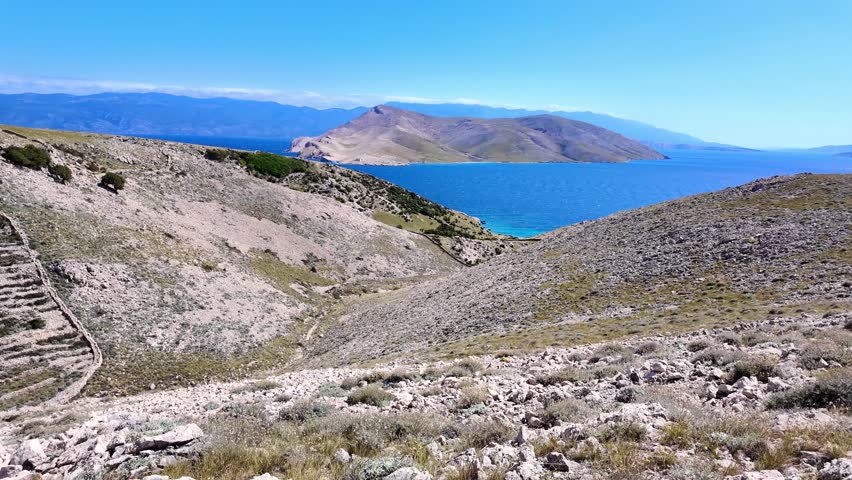Stunning coastal landscape with rolling hills and vibrant blue sea under clear skies. Krk island, Croatia.
