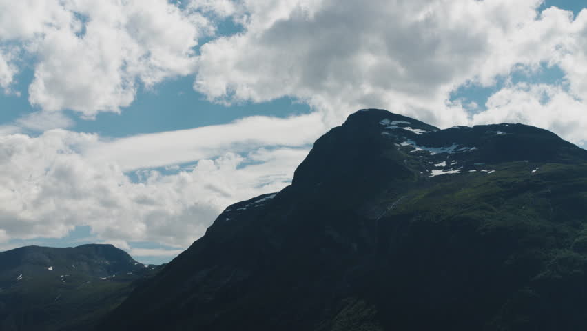 Wide shot of mountain peaks in Norway with clouds covering the sky on a bright sunny day