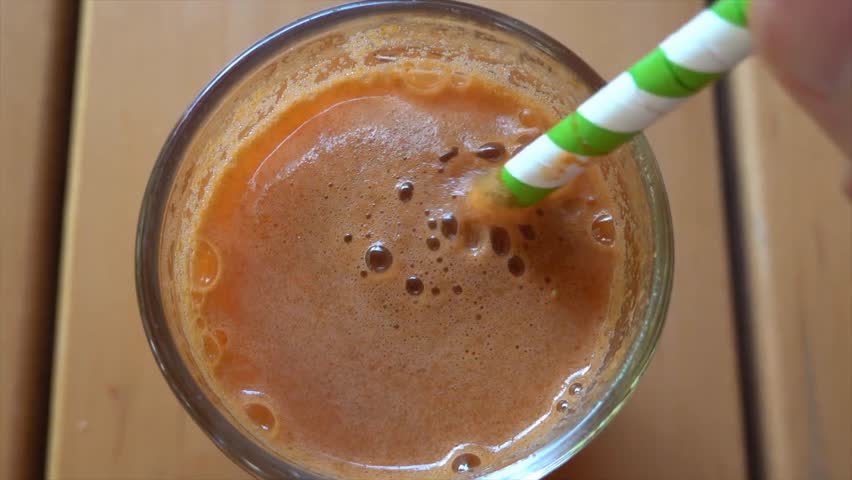 Man mixing a refreshing carrot and apple juice with a green and white striped straw, showcasing healthy eating and fresh organic beverage preparation.