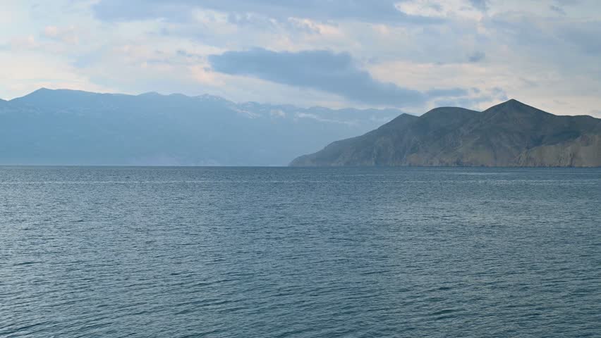 Tranquil coastal panorama with dramatic mountain range and cloudy sky at dusk. View of Prvić island, Croatia.