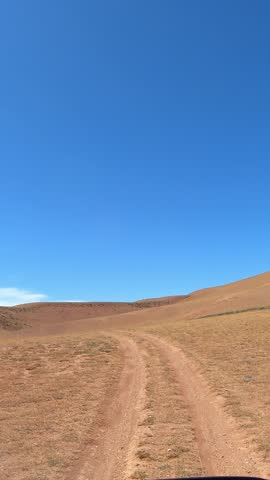 Vertical video of a car driving along a country road under blue sky. Altai desert and semi-desert environment.
