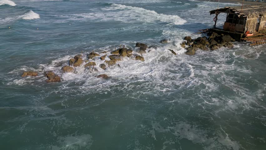 Aerial, panoramic view of the northern coast of the island of Crete. Waves crashing against the rocky pier near the town of Agia Marina and Platanias, Crete, Greece