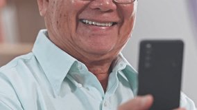 Asian smiling elderly man smartphone closeup light blue shirt casual indoor portrait warm expression senior man holding mobile phone selfie closeup of lower face and hand while video calling senior - Powered by Shutterstock - Get 15% off with code: PIKWIZARD15