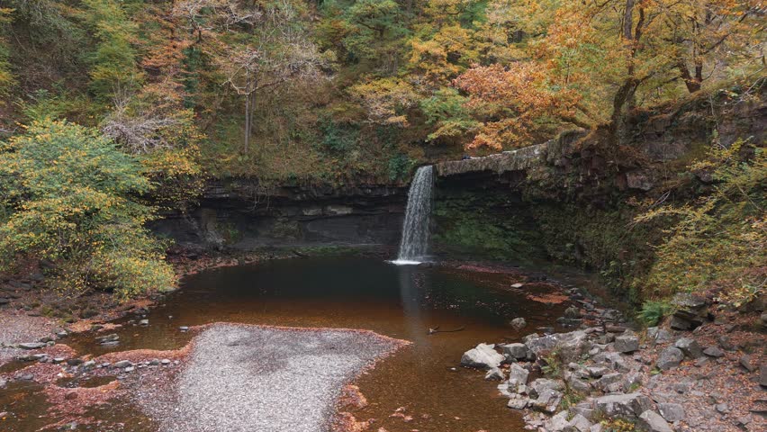 Autumnal forest scene with hiker beside a cascading waterfall in Brecon Beacons, Wales