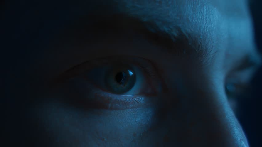 Close-up of a man wide-open eyes staring continuously at the screen in fear and astonishment. Addiction to social media, digital dependence and mindlessly doomscrolling 