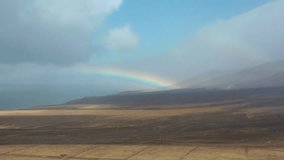 Natural landscape in Fuerteventura, Canary Islands  a dirt path through arid land facing the sea, with a colorful rainbow breaking through dramatic clouds. - Powered by Shutterstock - Get 15% off with code: PIKWIZARD15