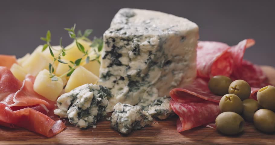 set of various meat and cheese snacks on wooden cutting board, closeup of delicatessen served for party