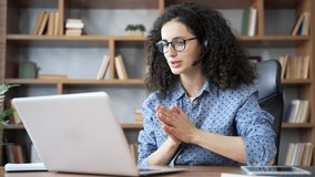 Confident woman in headset talking on video call using laptop sitting in home office. Female freelancer, tutor, coach or teacher has online meeting, training, consultation, course or webinar remotely - Powered by Shutterstock - Get 15% off with code: PIKWIZARD15