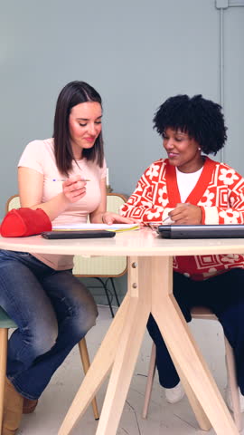 Two multiracial female students studying together at desk with books and notebooks, concept of education, teamwork, learning, diversity, friendship, focus, cooperation, knowledge and academic 