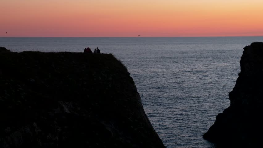 Silhouette people on rocks of Belle-Île at sunset. Slow motion 4K