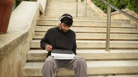 Young male student with headphones using a tablet while sitting on outdoor stairs - Powered by Shutterstock - Get 15% off with code: PIKWIZARD15