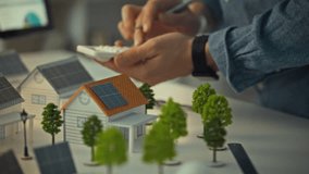 A design engineer is using a calculator and pen to assess data while planning solar panel installations on model houses. This activity takes place in a workspace focused on renewable energy solutions - Powered by Shutterstock - Get 15% off with code: PIKWIZARD15
