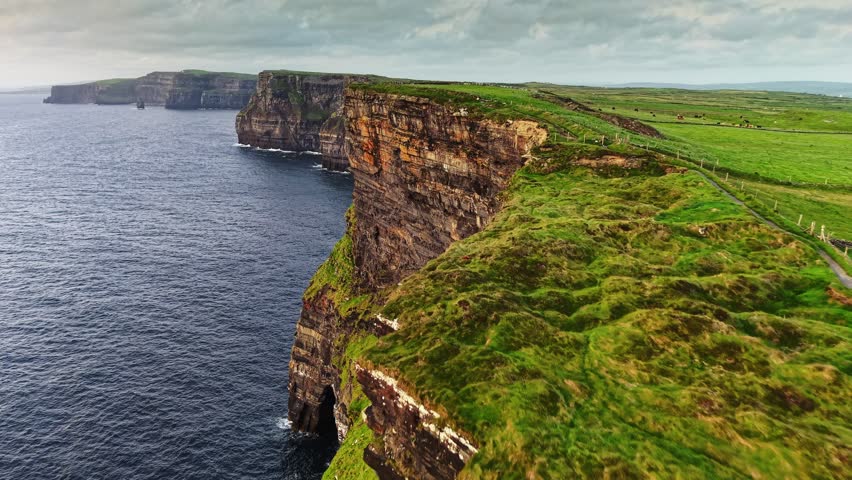 Aerial breathtaking cliffs of Moher in Ireland, County Clare. Flying over path near the edge of Cliff of Moher - one of the most popular tourist destinations in Ireland