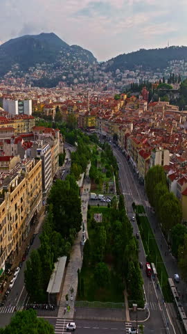  Aerial view of bustling beachfront promenade on sunny day. Beautiful panorama in Nice, France. Palm trees, old houses in old town azure sea and green hills. Summer in French Riviera