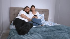A loving couple, relaxing in bed, exchanging interesting conversations and impressions, browsing social networks through a smartphone and spending quality leisure time together at home - Powered by Shutterstock - Get 15% off with code: PIKWIZARD15