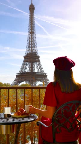 A beautiful woman in a red dress and a beret hat enjoys a breakfast with view of the Eiffel Tower in Paris, France