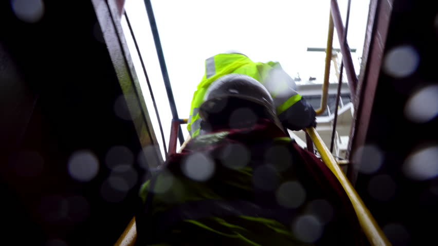 Team of sailors climbs narrow steps with careful synchronized rhythm. Camera captures drops falling between helmets and bright jackets