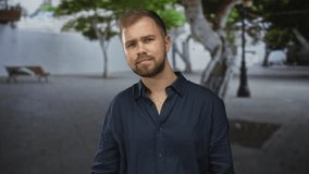 Man with beard tilts head and leans forward showing face and chest in an urban street plaza with trees, bench and lamp post; thoughtful calm. - Powered by Shutterstock - Get 15% off with code: PIKWIZARD15