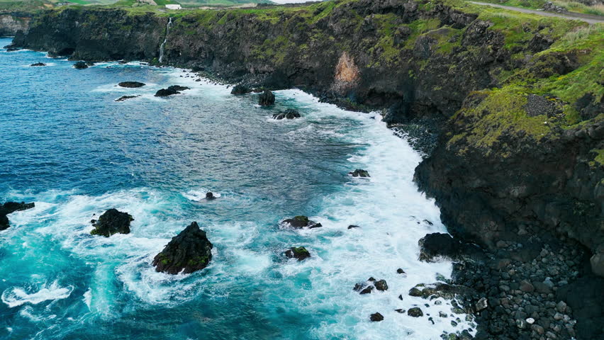 Aerial landscape of rugged lava cliffs and coastal reefs with bright green vegetation, Azores archipelago, Portugal