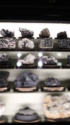 Vertical screen mineral specimens with metallic and crystal textures displayed in illuminated museum case geological collection showing natural formations and structure of earth minerals and stones