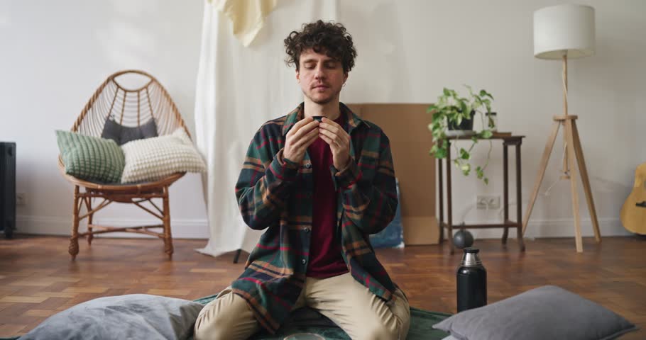 Zoom in portrait of guy trying tea from small Asian cup and smiling posing in bright apartment. Guy posing and drinking tea in Asian style at home