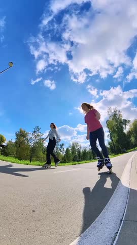 Two Caucasian women roller skating in a park. 