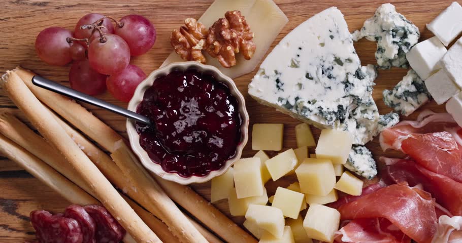 set of various meat and cheese snacks on wooden cutting board, closeup of delicatessen served for party
