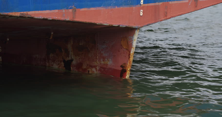 Steel hull of vessel rests in calm water with gleaming faintly draft marks. Cold geometry of sea engineering feels timeless and strong