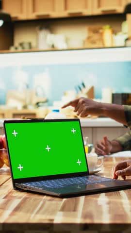 Vertical Video Chroma key next to black family enjoying breakfast at the kitchen table, with plates of omelettes, toast and fruits. Parents and kids laugh together, starting the day with delicious