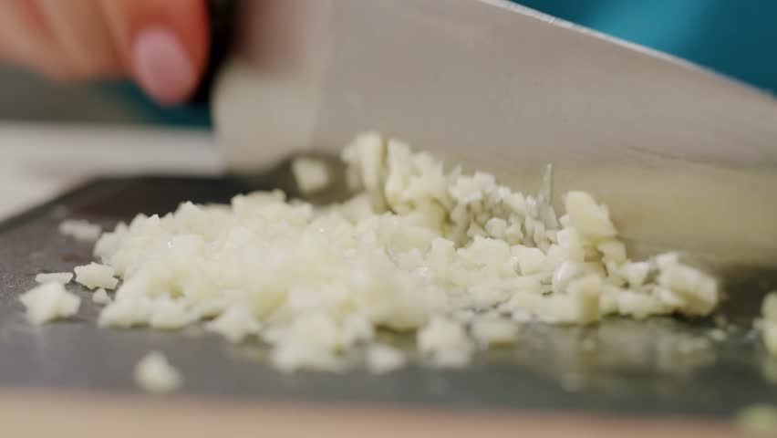 Woman chopping garlic on wooden cutting board at domestic kitchen, cut garlic with knife for curry. 