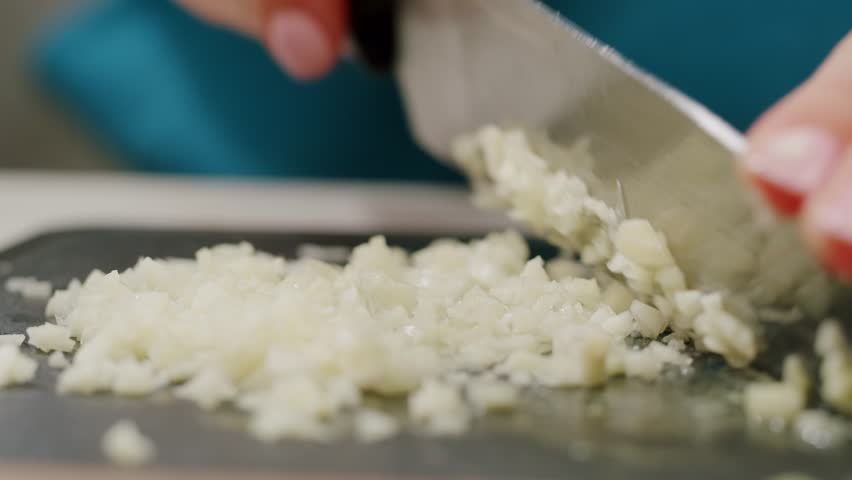 Woman chopping garlic on wooden cutting board at domestic kitchen, cut garlic with knife for curry. 
