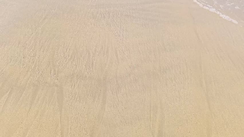 Close-up of Gentle Waves Lapping Golden Beach Sand from Overhead View.