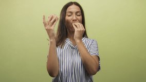 Hispanic young brunette woman holding cupcake with raised hands and smiling in green studio wearing striped shirt; joy celebration. - Powered by Shutterstock - Get 15% off with code: PIKWIZARD15