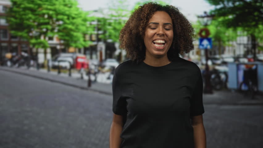 Woman cups hands to mouth shouting on a city street with fists clenched and mouth wide open; excitement celebration.